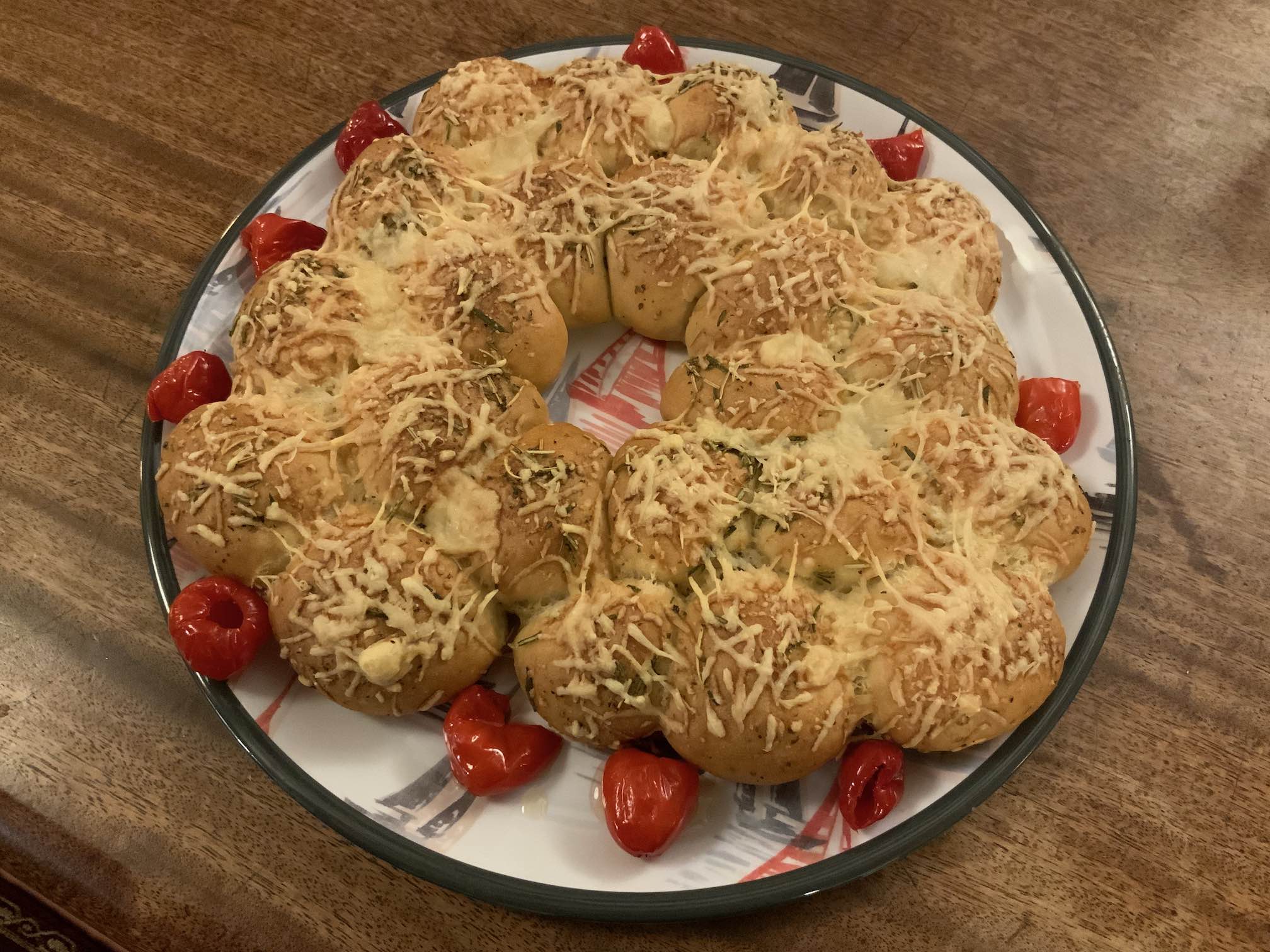 Photo of a large plate of bread balls topped with cheese and herbs, with will little peppers around the edge.