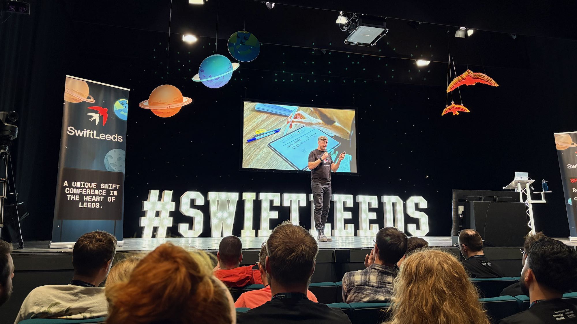 Photo of Adam on stage at the conference with some guy sketchnoting on screen behind.
