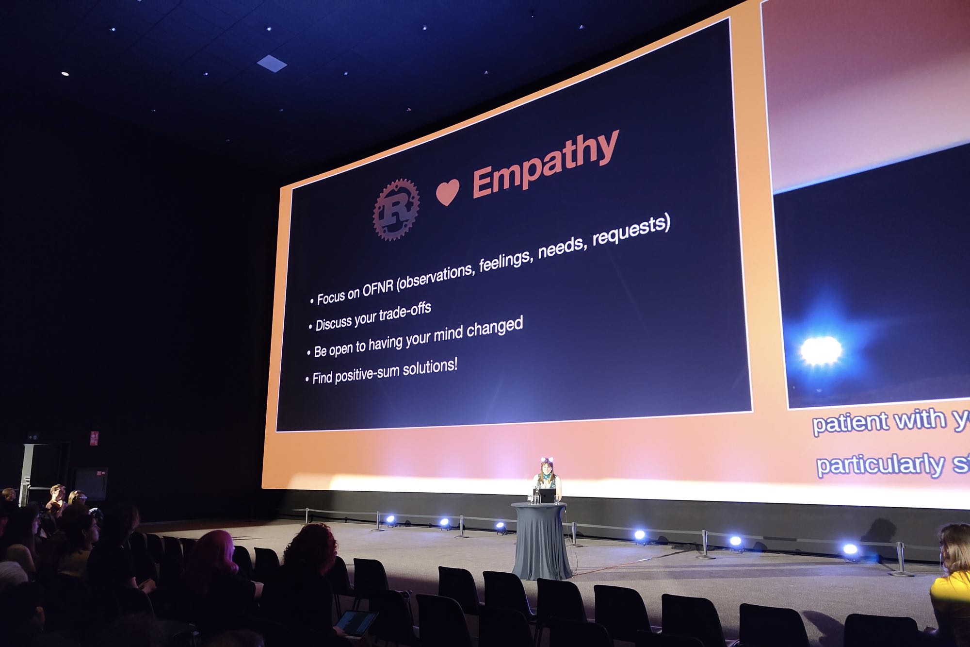 Photo of Taylor Cramer on stage with summary slide that says: Empathy; Focus on OFNR (observations, feelings, needs, requests); Discuss your trade-offs; Be open to having your mind changed; Find positive-sum solutions!